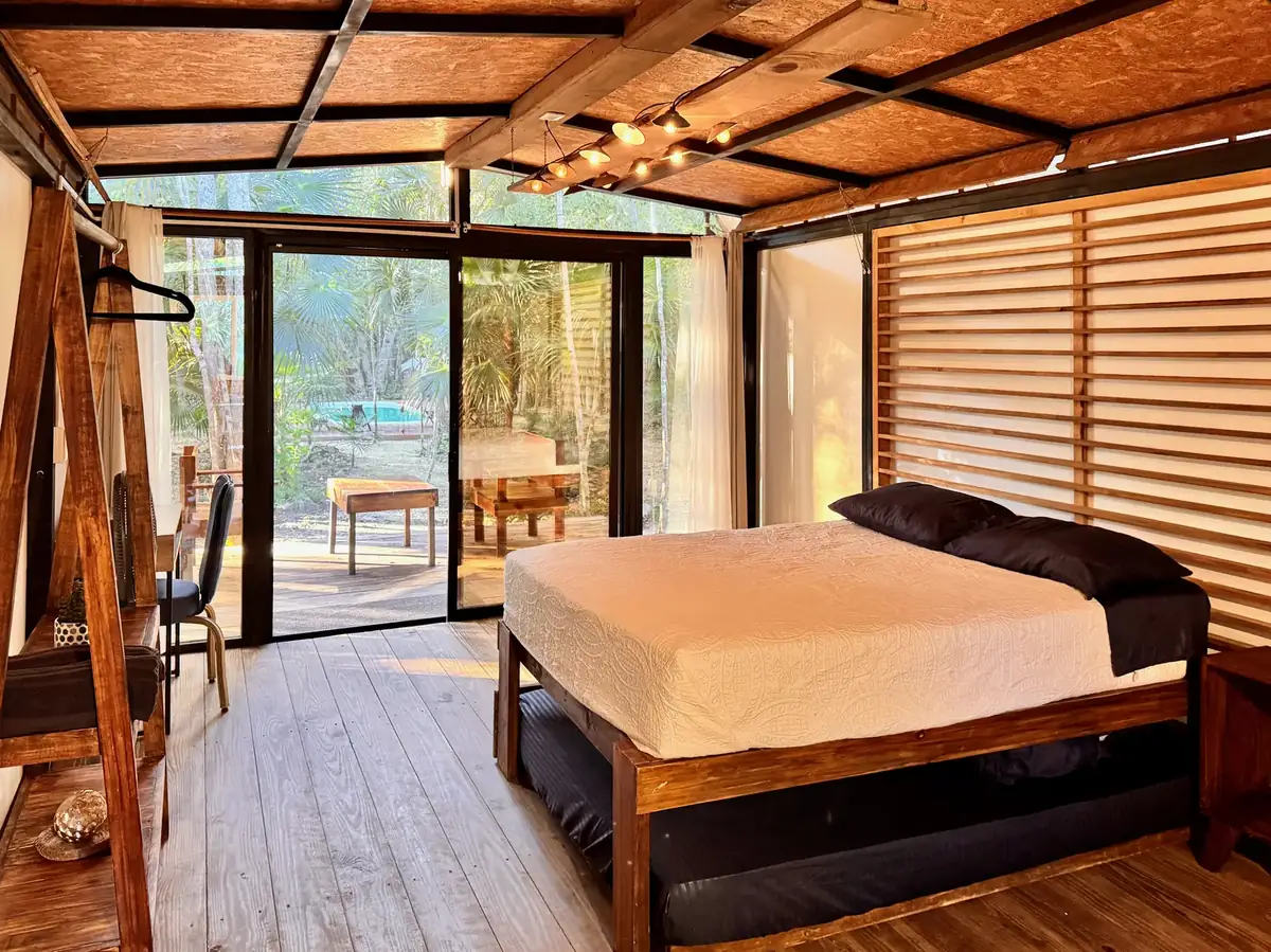 Inside a cabin, the bed facing a full wall of glass onto the jungle